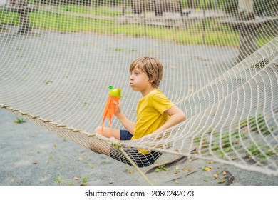 Practice Nets Playground. Boy Plays In The Playground Shielded With A Protective Safety Net. Concept Of Children On Line, Kid In Social Networks. Blurred Background, Blurred Motion Due To The Concept