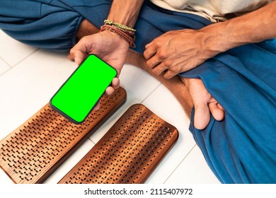 Practice of standing on nails. Man sitting in lotus position with phone on a light background. Wooden sadhu board with nails for sadhu practice