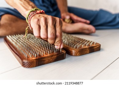 Practice of standing on nails. Man sitting in lotus position with wooden sadhu board with nails for sadhu practice. Man touching a nail on a board