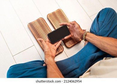 Practice of standing on nails. Man sitting in lotus position with phone on a light background. Wooden sadhu board with nails for sadhu practice