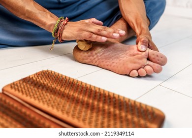 Practice of standing on nails. Sadhu wooden board with nails for sadhu practice. Man massaging his foot with a wooden massager after practicing standing on nails