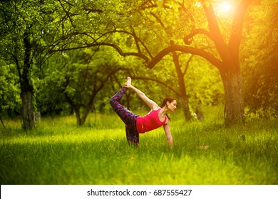 Practicing Yoga Asanas In Nature. Woman Practicing Cat Pose With Leg Seizure. Yoga Pose Marjaryasana. Toned Image.