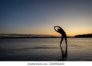 practicing yoga palm tree pose - sunrise silhouette of a man on a lake beach, Boyd Lake State Park in northern Colorado - Powered by Shutterstock