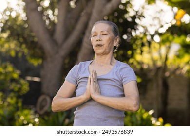 Practicing yoga, senior asian woman meditating outdoors with hands in prayer position. meditation, wellness, relaxation, mindfulness, fitness, spirituality - Powered by Shutterstock