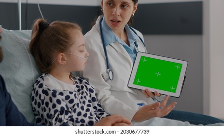 Practitioner doctor explaining disease expertise using mock up green screen chroma key tablet with isolated display in hospital ward. Little girl recovering medication treatment during examination