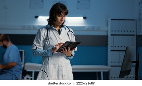 Practitioner doctor holding tablet computer checking patient report while typing medical expertise during night shift in hospital office. Physician woman in white coat working at health care treatment - Powered by Shutterstock