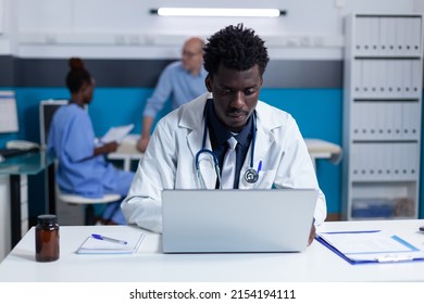 Practitioner Expert Using Laptop In Healthcare Facility Cabinet. Clinic Specialist Uploading Critical Patient Disease Records And Prescribed Medications To Clinic Database.