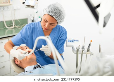 Practitioner female dentist drilling tooth to male patient businessman in dental studio - Shutterstock ID 2314799595