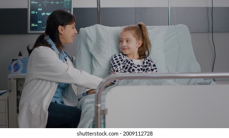 Practitioner Pediatrician Woman Doctor Explaining Recovery Treatment To Sick Child Giving High Five During Medicine Examination In Hospital Ward. Hospitalized Kid Recovering After Medical Surgery