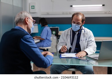 Practitioner Putting Medical Seal On Prescription Paper To Give Health Care Medicine To Senior Man In Office. Physician Using Stamp On Checkup Visit Report During Coronavirus Pandemic.