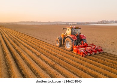 PRAGUE , CZECH REPUBLIC - MARCH 18 2022: Heavy tractor uses plow to make beds for planting potatoes in agricultural field. Powerful machine operates at farm on sunny day aerial view