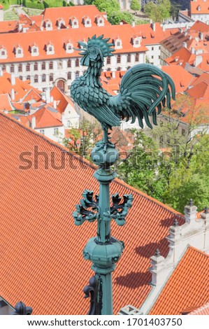 Prague, Czech Republic - Metal sculpture of a rooster on the spire of one of the towers of St. Vitus Cathedral against the background of bright tiled roofs