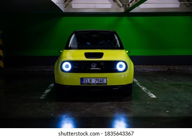 Prague, Czech Republic - October 02, 2020. Yellow Green Electric Honda E Parked In Dark Industrial Parking Spot With Green Key Background - Front View With Lights On