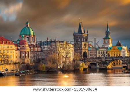 Prague, Czech Republic - The world famous Charles Bridge (Karluv most) with St. Francis of Assisi Church and clocktower with beautiful golden sunset lights and moving orange clouds on winter afternoon
