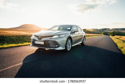 Prague, Czechia, 07-10-2020: Brand new Toyota Camry hybrid 2020 is driven at empty countryside asphalt road at sunset. Car in the ride.
