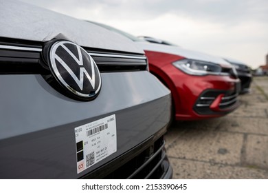 PRAGUE, CZECHIA – MAY 6, 2022: Logo of VW of german Volkswagen Group on the front of gray Golf car at a parking area before sale. New car with protective equipment. Red Polo behind. Coudy.