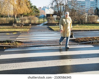 PRAGUE, CZECHIA - Older woman crossing road on zebra markings. In the country transit cars are always yielding the right of way to pedestrians on roadsigns without traffic light. Jan 3, 2022