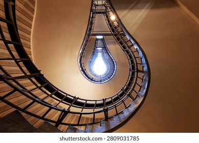 Prague staircase forms the visual illusion of a glowing light bulb, with curved railings and dramatic symmetry creating a striking abstract architectural composition.