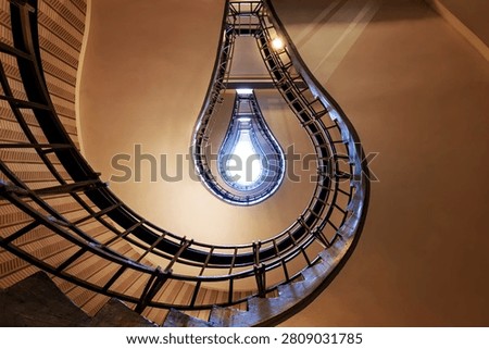 Prague staircase forms the visual illusion of a glowing light bulb, with curved railings and dramatic symmetry creating a striking abstract architectural composition.