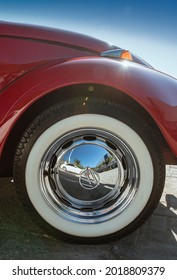 Praia Grande, São Paulo - Brazil - July 25, 2021: Partial view of the wheel of a red Beetle. Tire with white stripe and chrome hubcap glowing in sunny day with blue sky.

