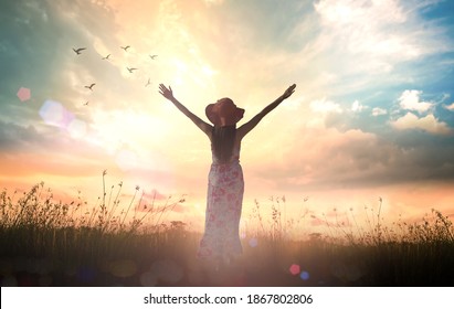 Praise And Worship God Concept: Silhouette Of Healthy Woman Raised Hands At Meadow Sunset Background