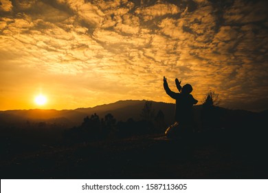 Pray of man kneeling down and lift hands at sunset background. christian silhouette concept.