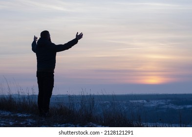 Pray. Repentance. Silhouetted men on a background of blue sky and sunset. Kneeling Prayer to God. Glorification. Praising God. A man with his hands up. Worship God