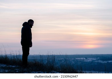 Pray. Repentance. Silhouetted men on a background of blue sky and sunset. Kneeling Prayer to God. Glorification. Praising God. A man with his hands up. Worship God