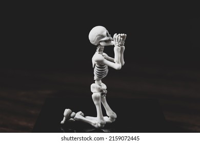 Pray skeleton figurine. Prayer figure on knees on dark background. Kneeling humility, promise, sadness, pleading, forgiveness belief and sorrow concept