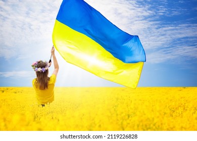 Pray for Ukraine. Child with Ukrainian flag in a field of yellow flowers. Little girl waving national flag praying for peace. Happy kid celebrating Independence Day.