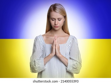 Pray for Ukraine. Young woman with clasped hands praying against Ukrainian national flag