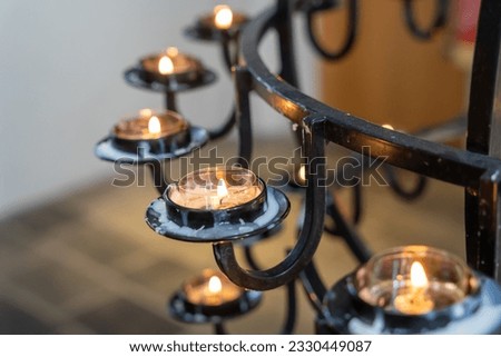 Prayer candles in black chandelier burning in church