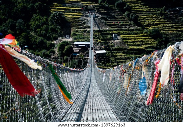 Prayer\
flags and trekkers in hanging bridge in\
Nepal