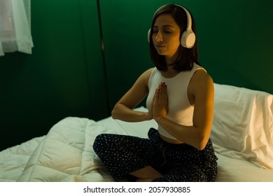 Prayer position. Calm young woman doing a meditation routine while listening to relaxing music with headphones in bed - Powered by Shutterstock