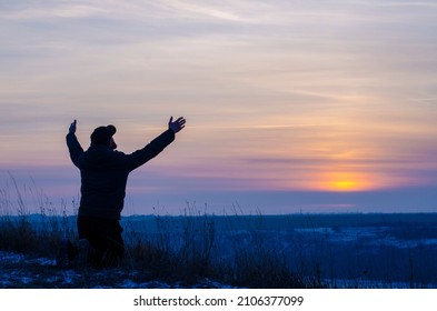 Prayer. Repentance. Silhouetted men on a background of blue sky and sunset. Kneeling Prayer to God. Glorification. Praising God. Jesus is risen. Man with raised hands
