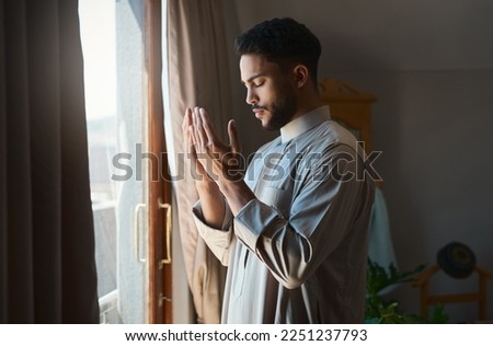 Prayer is the surrender of all fears. Shot of a young muslim man praying in the lounge at home.