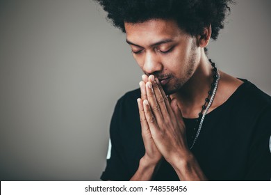 Praying african american man hoping for better. Asking God for good luck, success, forgiveness. Power of religion, belief, worship. Holding hands in prayer, eyes closed.