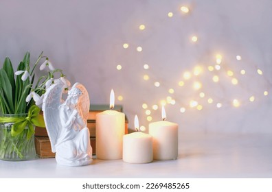 praying angel, candles, flowers and books on table, abstract light background. Christmas or Easter holiday concept. Religious church holiday. symbol of faith in God, Christianity Feast