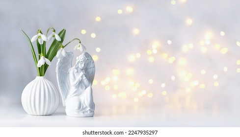 Praying angel figurine and snowdrops flowers on table, abstract light background. symbol of faith in God, christianity. Religious church holiday, Easter, Feast of Annunciation to Blessed Virgin Mary