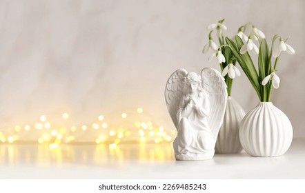 Praying angel figurine, snowdrops flowers on table, abstract light background. Religious church holiday. symbol of faith in God, christianity. Easter, Feast of Annunciation to the Blessed Virgin Mary