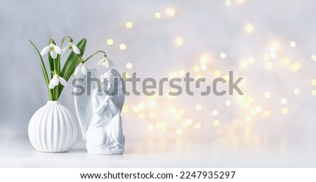 Praying angel figurine and snowdrops flowers on table, abstract light background. symbol of faith in God, christianity. Religious church holiday, Easter, Feast of Annunciation to Blessed Virgin Mary