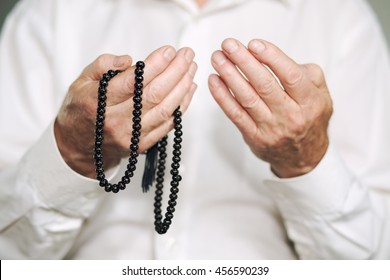 Praying hands of an old man holding rosary beads