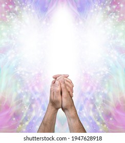 Praying for help from the Angelic Realms - male hands clasped in prayer position against a bright white Angel form and beautiful pale multicoloured spiritual energy behind
