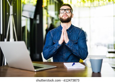Praying for success. Front view of thoughtful young man holding hands on chin and looking at the laptop while sitting at his working place in office - Shutterstock ID 612473873