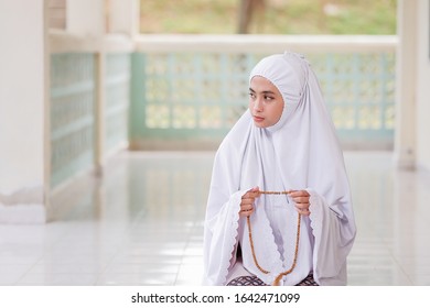 Praying woman with traditional Islamic beads in hand and kneeling in a mosque.