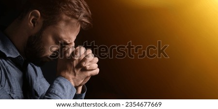 Praying young man on dark background with space for text
