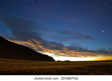 Pre Dawn Sky With Stars Above Bank Of Clouds With Emerging Sunlight Over Plain And Hill.