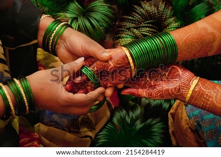 At a pre wedding ceremony a lady bangle seller is putting green glass bangles on the henna decorated hands of  a maharashtrian bride. They 
symbolize fertility and prosperity in Indian culture.      