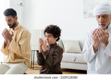 Preadolescent Arabian Kid With Closed Eyes Praying Near Multiethnic Men At Home