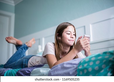 Pre-adolescent teen girl texting on a smartphone lying in bed at home. Candid indoor photo withFocus on the foreground and copy space - Shutterstock ID 1169505235